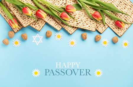Jewish holiday Passover greeting card concept with matzah, nuts, tulip and daisy flowers on blue...