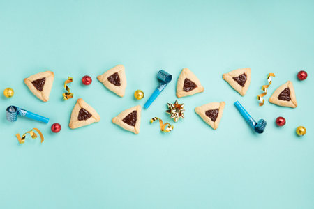 Purim celebration jewish holiday concept. Tasty hamantaschen cookies, Triangular pastry, Carnival mask, noisemaker, sweet candies and festive party decor on mint green background, Top view, copy spaceの写真素材