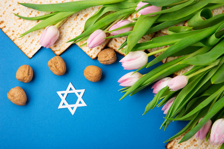 Jewish holiday Passover greeting card concept with matzah, nuts, tulip flowers on blue table Seder...