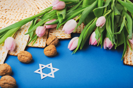 Jewish holiday Passover greeting card concept with matzah, nuts, tulip flowers on blue table Seder...
