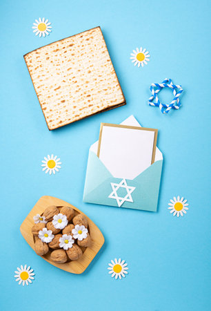 Jewish holiday Passover greeting card concept with matzah, nuts, spring flowers on blue table. Seder Pesach spring holiday background, top view, copy space.の写真素材