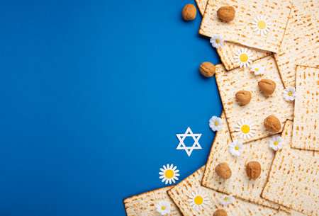 Jewish holiday Passover greeting card concept with matzah, nuts, spring flowers on blue table. Seder Pesach spring holiday background, top view, copy space.の写真素材