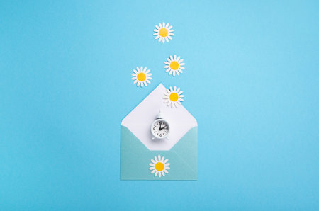 White alarm clock and Daisy Flowers on blue background. Spring forward, Time Change, Daylight Saving Time Ends, Changing the time on the watch to spring time, Summer back concept.の写真素材