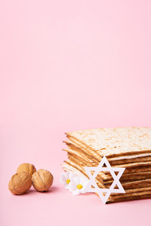Jewish holiday Passover greeting card concept with matzah, nuts, spring daisy flowers on pink table. Seder Pesach spring holiday background, copy space.の写真素材