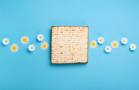 Jewish holiday Passover greeting card concept with matzah, nuts, spring flowers on blue table. Seder Pesach spring holiday background, top view, copy space.の写真素材