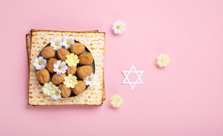 Jewish holiday Passover greeting card concept with matzah, Star of David, spring daisy flowers, walnuts on pink table. Seder Pesach spring holiday background, copy space.の写真素材
