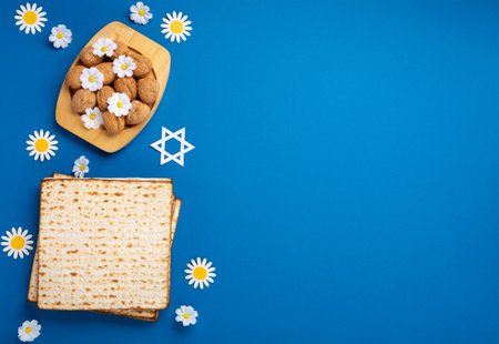 Jewish holiday Passover greeting card concept with matzah, nuts, spring flowers on blue table. Seder...