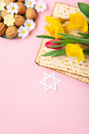 Jewish holiday Passover greeting card concept with matzah, nuts, spring daisy flowers on pink table. Seder Pesach spring holiday background, copy space.の写真素材