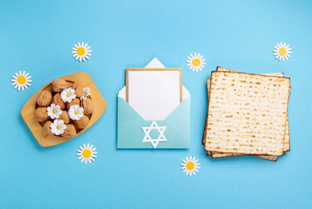 Jewish holiday Passover greeting card concept with matzah, walnuts, daisy flowers and empty envelope on blue table. Seder Pesach spring holiday background, top view, copy space.の写真素材