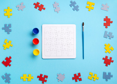 World Autism Awareness Day or month concept. Creative design for April 2. White puzzles, symbol of awareness for autism spectrum disorder and colorful paints on blue background. Top view, copy space.の写真素材