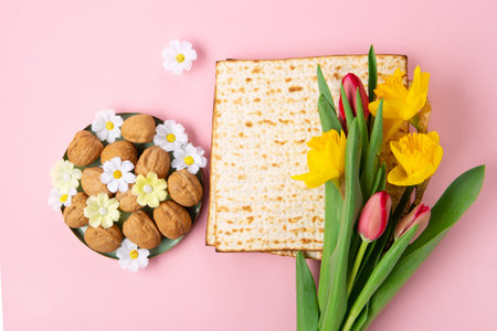 Jewish holiday Passover greeting card concept with matzah, Star of David, spring yellow daffodil, tulips, daisy flowers, walnuts on pink table. Seder Pesach spring holiday background, copy space.の写真素材