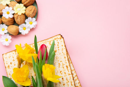 Jewish holiday Passover greeting card concept with matzah, Star of David, spring yellow daffodil, tulips, daisy flowers, walnuts on pink table. Seder Pesach spring holiday background, copy space.の写真素材
