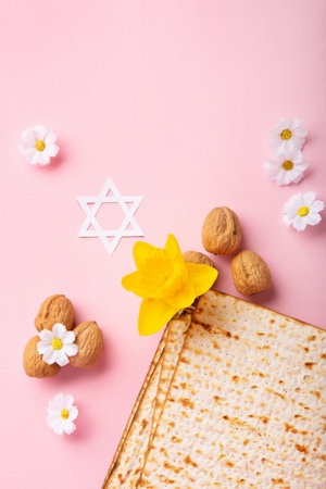 Jewish holiday Passover greeting card concept with matzah, Star of David, spring yellow daffodil, daisy flowers, walnuts on pink table. Seder Pesach spring holiday background, copy space.の写真素材