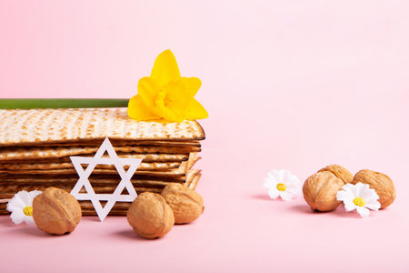 Jewish holiday Passover greeting card concept with matzah, Star of David, spring yellow daffodil, daisy flowers, walnuts on pink table. Seder Pesach spring holiday background, copy space.の写真素材