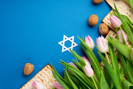 Jewish holiday Passover greeting card concept with matzah, nuts, tulip flowers on blue table. Seder Pesach spring holiday background, top view, copy space.の写真素材