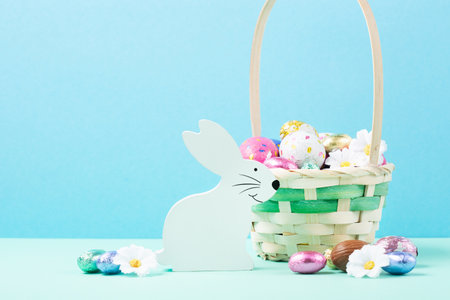 Easter Basket, Sweet Colorful Chocolate Easter Eggs, daisy flowers on pastel blue mint background. Happy Easter greeting card, Egg hunt concept, copy space.の写真素材