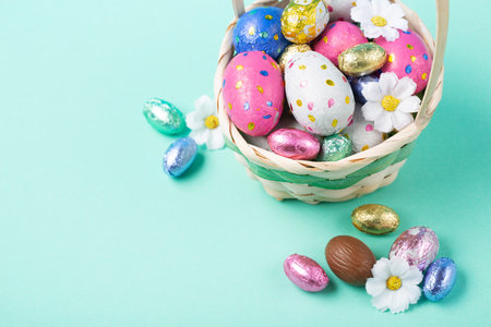 Easter Basket, Sweet Colorful Chocolate Easter Eggs, daisy flowers on pastel blue mint background. Happy Easter greeting card, Egg hunt concept, copy space.の写真素材