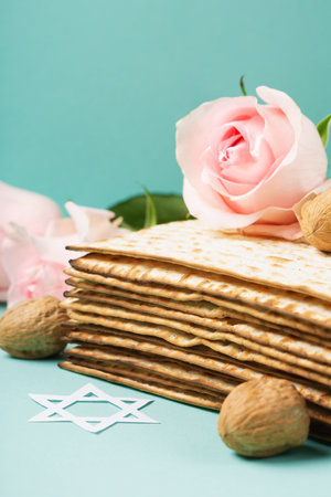 Jewish holiday Passover greeting card concept with matzah, Star of David, spring flowers, walnuts on blue mint table. Seder Pesach spring holiday background, copy space.の写真素材