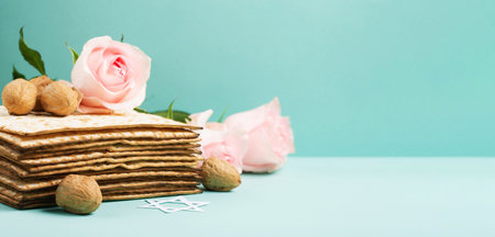 Jewish holiday Passover greeting card concept with matzah, Star of David, spring flowers, walnuts on blue mint table. Seder Pesach spring holiday background, copy space.の写真素材