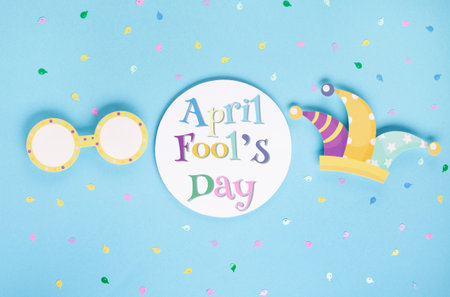 April Fool's Day holiday card with Jester hat, confetti and funny glasses on blue background, top view. International Day of Laughter. Concept for greeting cards, banners, flyers.の写真素材