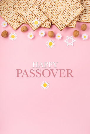 Jewish holiday Passover greeting card concept with matzah, nuts, tulip and daisy flowers on pink table. Seder Pesach spring holiday background, top view, copy space.の写真素材