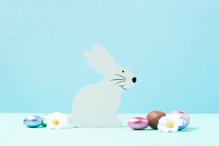 White Wooden Bunny, Sweet Colorful Easter Eggs, daisy flowers on pastel blue mint background. Happy...