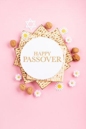 Jewish holiday Passover greeting card concept with matzah, nuts and spring daisy flowers on pink table. Seder Pesach spring holiday background, top view, copy space.の写真素材