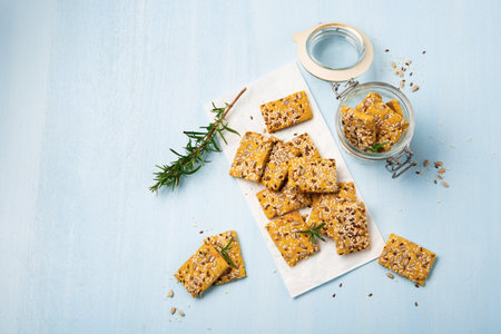 Gluten free Homemade Crackers and rosemary on Blue background. Healthy eating, ancient grain food, dieting, balanced food concept. Cereals gluten-free, millet, quinoa, flax seeds, sunflower seeds.の写真素材