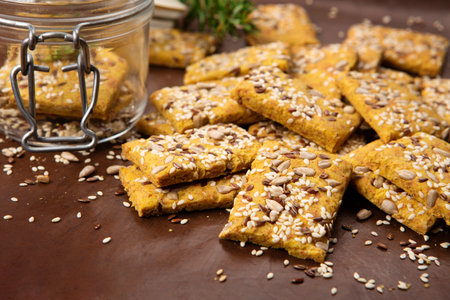 Gluten free Homemade Crackers and rosemary on brown background. Healthy eating, ancient grain food, dieting, balanced food concept. Cereals gluten-free, millet, quinoa, flax seeds, sunflower seeds.の写真素材