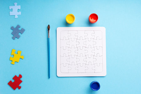 World Autism Awareness Day or month concept. Creative design for April 2. White puzzles, symbol of awareness for autism spectrum disorder and colorful paints on blue background. Top view, copy space.の写真素材