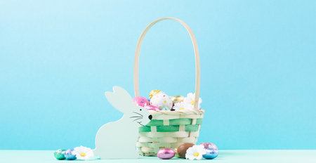 White Wooden Bunny, Easter Basket, Sweet Chocolate Easter Eggs, daisy flowers on pastel blue mint background. Happy Easter greeting card, Egg hunt concept, copy space.の写真素材