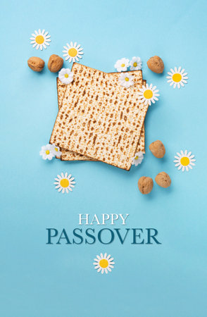 Jewish holiday Passover greeting card concept with matzah, nuts and daisy flowers on blue table. Seder Pesach spring holiday background, top view, copy space.の写真素材
