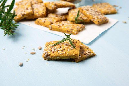 Gluten free Homemade Crackers and rosemary on Blue background. Healthy eating, ancient grain food, dieting, balanced food concept. Cereals gluten-free, millet, quinoa, flax seeds, sunflower seeds.の写真素材
