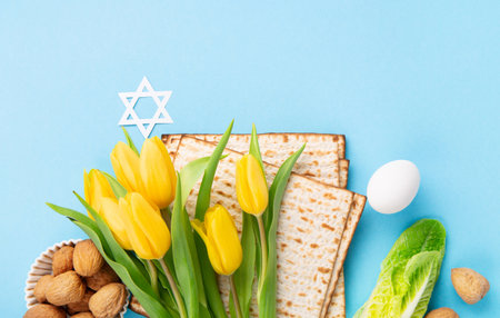 Jewish holiday Passover greeting card concept with matzah matzoh (jewish holiday bread), walnuts, yellow tulip flowers on blue table. Seder Pesach spring holiday background, copy space.の写真素材