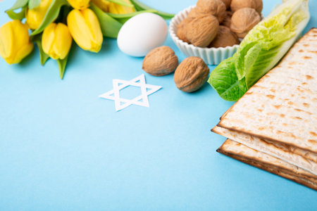 Jewish holiday Passover greeting card concept with matzah matzoh (jewish holiday bread), walnuts, yellow tulip flowers on blue table. Seder Pesach spring holiday background, copy space.の写真素材