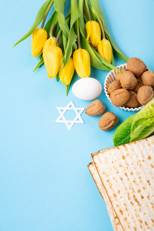 Jewish holiday Passover greeting card concept with matzah matzoh (jewish holiday bread), walnuts, yellow tulip flowers on blue table. Seder Pesach spring holiday background, copy space.の写真素材