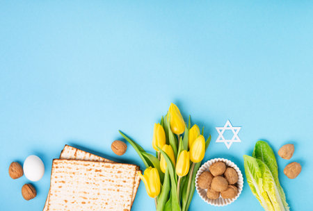 Jewish holiday Passover greeting card concept with matzah matzoh (jewish holiday bread), walnuts, yellow tulip flowers on blue table. Seder Pesach spring holiday background, copy space.の写真素材
