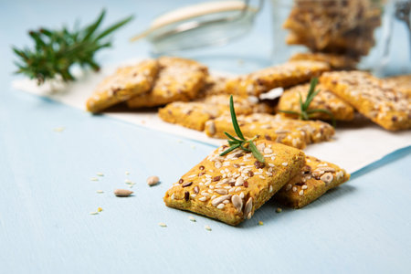 Gluten free Homemade Crackers and rosemary on Blue background. Healthy eating, ancient grain food, dieting, balanced food concept. Cereals gluten-free, millet, quinoa, flax seeds, sunflower seeds.の写真素材