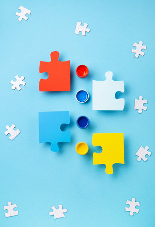 World Autism Awareness Day or month concept. Creative design for April 2. White puzzles, symbol of awareness for autism spectrum disorder and colorful paints on blue background. Top view, copy space.の写真素材