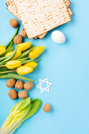 Jewish holiday Passover greeting card concept with matzah matzoh (jewish holiday bread), walnuts, yellow tulip flowers on blue table. Seder Pesach spring holiday background, copy space.の写真素材