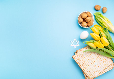 Jewish holiday Passover greeting card concept with matzah matzoh (jewish holiday bread), walnuts, yellow tulip flowers on blue table. Seder Pesach spring holiday background, copy space.の写真素材