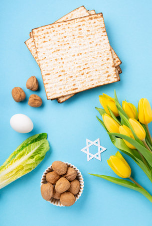 Jewish holiday Passover greeting card concept with matzah matzoh (jewish holiday bread), walnuts, yellow tulip flowers on blue table. Seder Pesach spring holiday background, copy space.の写真素材