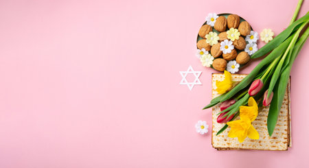 Jewish holiday Passover greeting card concept with matzah, Star of David, spring yellow daffodil, tulips, daisy flowers, walnuts on pink table. Seder Pesach spring holiday background, copy space.の写真素材