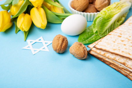 Jewish holiday Passover greeting card concept with matzah matzoh (jewish holiday bread), walnuts, yellow tulip flowers on blue table. Seder Pesach spring holiday background, copy space.の写真素材