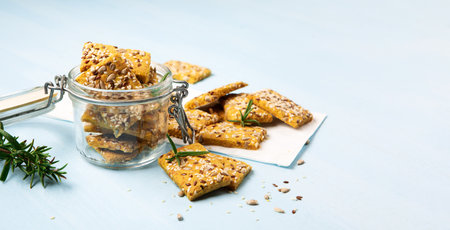 Gluten free Homemade Crackers and rosemary on Blue background. Healthy eating, ancient grain food, dieting, balanced food concept. Cereals gluten-free, millet, quinoa, flax seeds, sunflower seeds.の写真素材