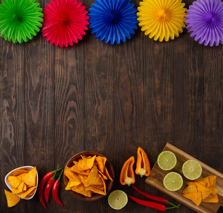 Cinco de Mayo (Fifth of May) celebration concept. Mexican background fiesta with Traditional Mexican nachos chips, red chili peppers, green lime on dark wooden background. Top view, copy space.の写真素材