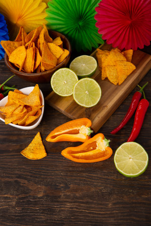 Cinco de Mayo (Fifth of May) celebration concept. Mexican background fiesta with Traditional Mexican nachos chips, red chili peppers, green lime on dark wooden background. Top view, copy space.の写真素材