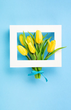 Mothers Day, International Womens Day, Valentines Day greeting card background. Holiday spring yellow tulip flowers bouquet on blue table, top view copy space.の写真素材