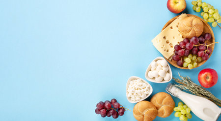 Happy Shavuot festive card, Jewish religious holiday concept. Dairy products, fruits, cheese, bread, milk bottle on blue background. Flat lay, top view, copy space.の写真素材
