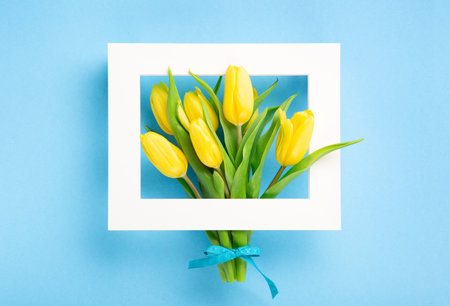 Mothers Day, International Womens Day, Valentines Day greeting card background. Holiday spring yellow tulip flowers bouquet on blue table, top view copy space.の写真素材